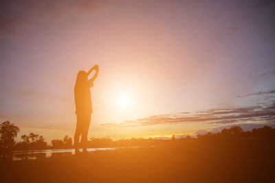 Silhouette woman standing on land against sky during sunset