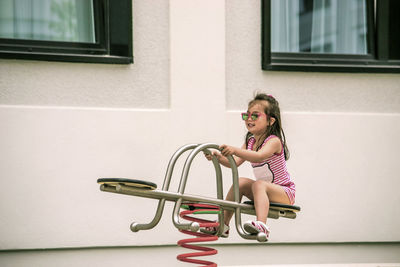 Full length of girl playing on seesaw by house