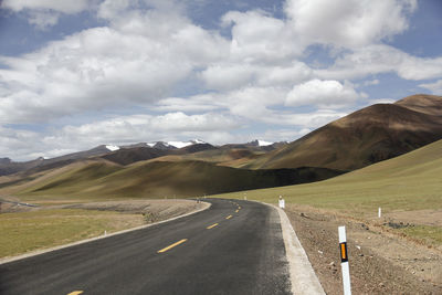 A flat, wide asphalt road leads to the beautiful and spectacular snow mountains in the distance