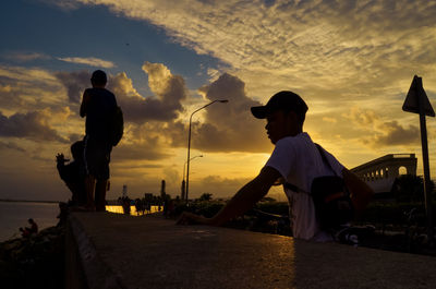 Silhouette man standing on street against sky during sunset