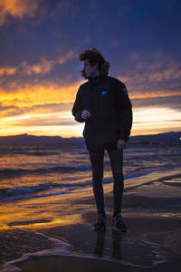 Full length of young man standing at beach during sunset