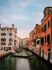 Venetian gondola as it sails on characteristic canal with colorful buildings at sunset