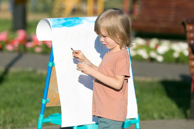 Side view of cute boy painting in park