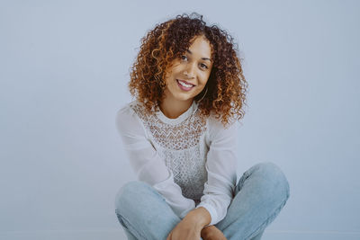 Portrait of smiling young woman sitting against wall