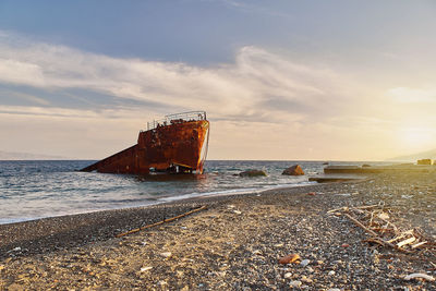 Abandoned ship on beach against sky during sunset