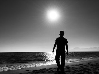 Rear view of silhouette man walking on beach against clear sky