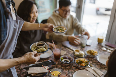 Male waiter serving dumplings to friends at restaurant