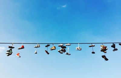 Low angle view of shoes hanging on cable against blue sky