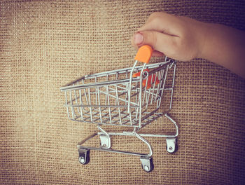 Cropped hand holding toy shopping cart on burlap