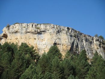 Low angle view of rocky mountain against clear blue sky