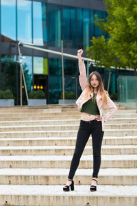 Full length portrait of young woman standing with arm raised on steps