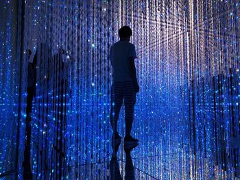 Rear view of man standing against illuminated light at night