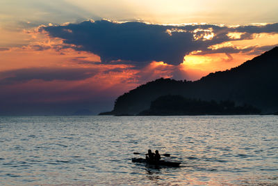 Silhouette men in boat on sea against sky during sunset