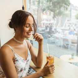 Smiling young woman sitting with drink on table at restaurant