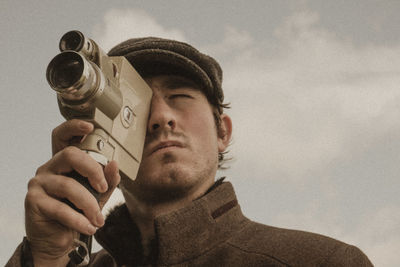 Man looking through vintage camera against sky