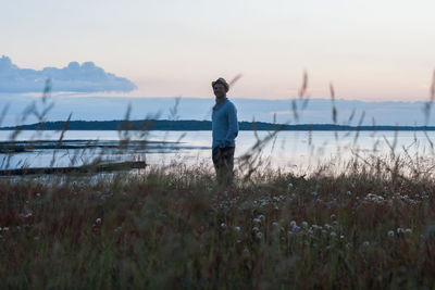 Portrait of mid adult man standing at lakeshore against clear sky during sunset