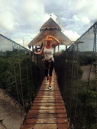 Full length of woman walking on rope bridge against cloudy sky