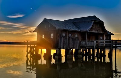 Wooden house by lake against sky during sunset