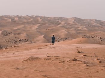 Man standing on sand dune in desert against sky