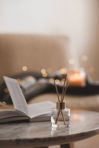 Bamboo sticks in bottle with scented candles and open book on marble table closeup