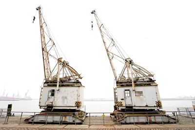 Cranes at harbor against sky