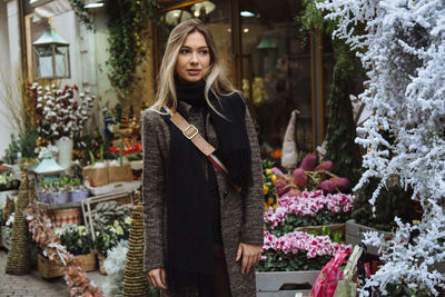 Thoughtful woman standing against flower shop in city