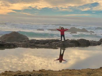 Woman with arms outstretched standing on rock at beach during sunset