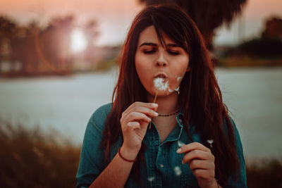 Portrait of beautiful young woman drinking water at lake during sunset