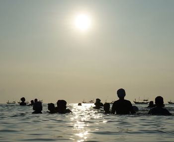 Silhouette people swimming in sea against clear sky