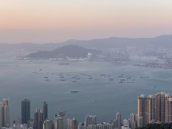 Sea by city buildings against sky during sunset