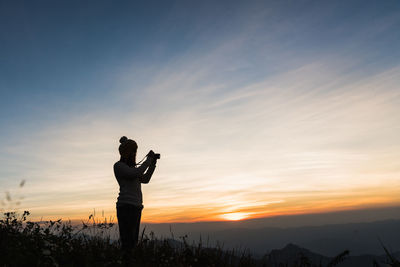 Silhouette woman photographing at sunset