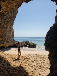 Rear view of woman standing at beach against sky