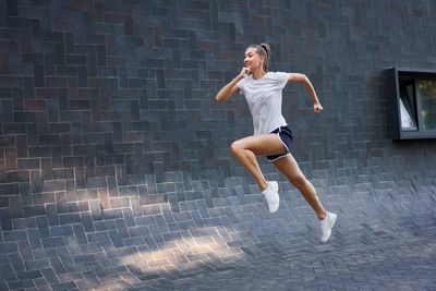 Full length of woman jumping against wall