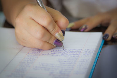 Cropped hand of woman with painted fingernails writing in book