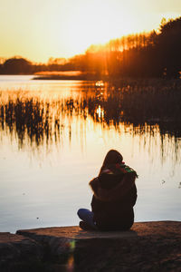 Woman sitting on lake against sky during sunset