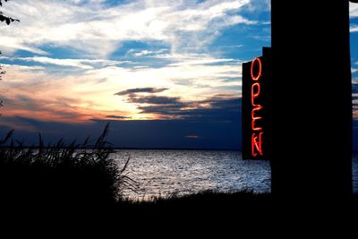 Sign board on beach against sky during sunset