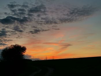 Silhouette trees on field against orange sky