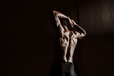 Male athlete with hands behind head standing in front gray wall during sunset