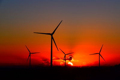 Silhouette wind turbines on field against sky during sunset