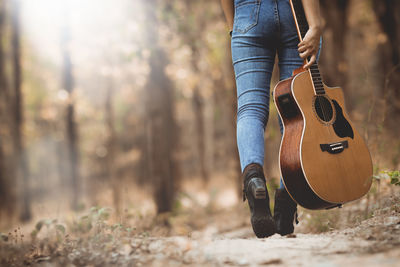 Low section of woman holding guitar while walking in forest