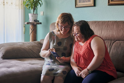 Adult woman and her sister with down syndrome look at a phone at home