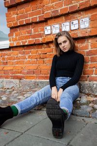 Portrait of young woman sitting against brick wall