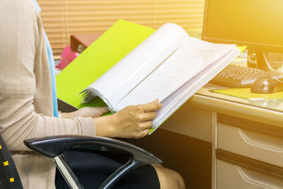 Midsection of businesswoman reading file while sitting at desk in office