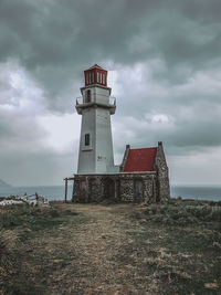 Lighthouse on field by building against sky