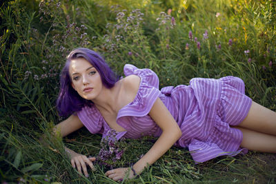 Teenage girl with dyed purple hair and a nose piercing in the grass  of flowers and in a short dress