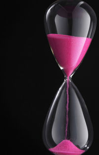 Close-up of hourglass with pink sand against black background