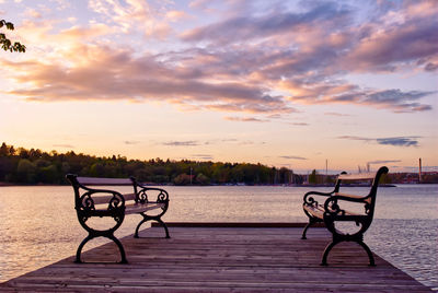 Empty bench against sea against sky during sunset