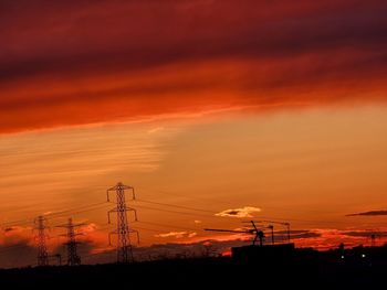 Silhouette electricity pylon against dramatic sky during sunset