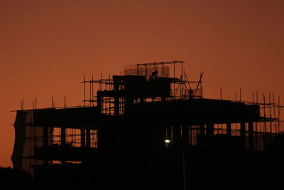 Silhouette built structure by sea against orange sky at sunset