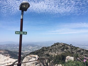 Low angle view of road sign on street light with mountain in background against blue sky